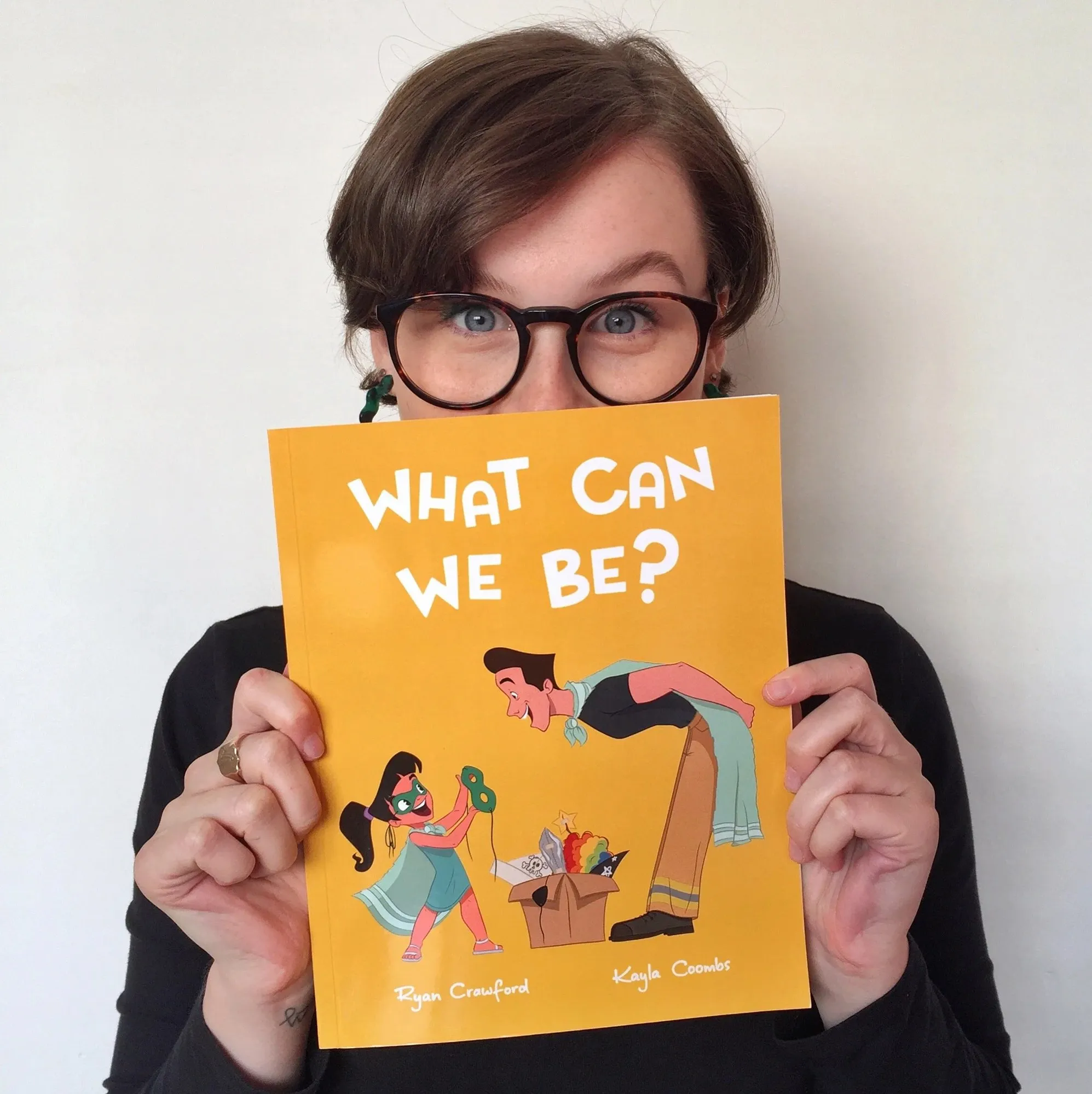 Kayla Coombs holding a copy of What Can We Be? up to her face